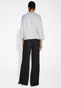 Maglione grigio con texture e colletto scialle, abbinato a pantaloni neri a gamba larga. Dettagli riflettenti sulla superficie del maglione.