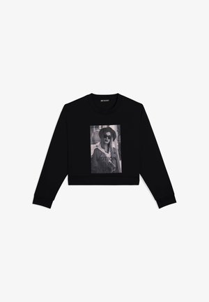 Felpa nera a maniche lunghe con una grande stampa grafica in bianco e nero con il testo "MOTION IS A THING" e una modella che indossa occhiali da sole.