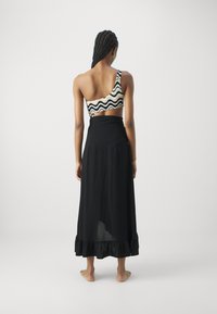 Eén-schouder zwart-wit bikini top met golfpatroon, gecombineerd met een vloeiende zwarte maxi rok met een ruchesrand.