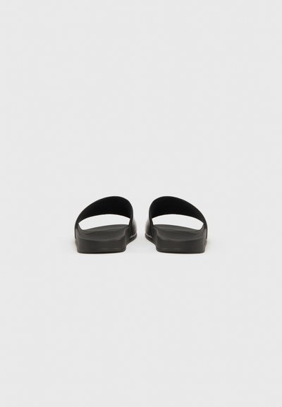 Sandales slides en caoutchouc noir au design minimaliste, avec une large bride sur le dessus et une forme plate à bout ouvert.