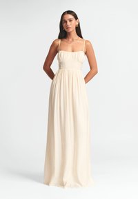 Vestido maxi de tela color crema claro, con tirantes ajustables, un corsé entallado con pliegues y una falda fluida con un acabado texturizado.