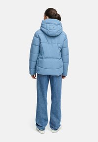 Ljusblå puffjacka med stor huva, kviltad textur och ribbade detaljer. Bärs med raka jeans i denim och vita sneakers.