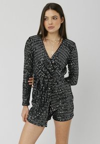 Robe courte noire avec des manches longues, design enveloppant, et rayures verticales en sequins argentés. Elle présente un décolleté en V profond et une taille froncée.