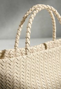 Sac fourre-tout en cuir tressé beige avec deux poignées tressées sur un fond uni et neutre.