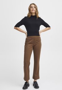 Haut noir à col montant côtelé avec des manches courtes, associé à un pantalon large marron et des mocassins noirs. Design simple, texture lisse.