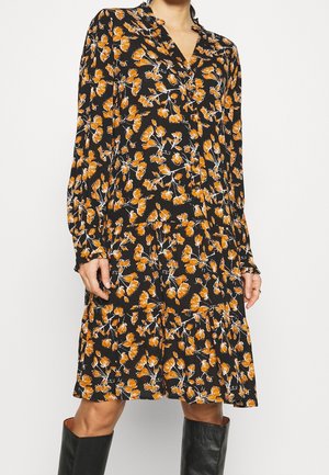 Sort langærmet kjole med orange blomsterprint, V-hals og knælængde, båret med sorte knæhøje støvler.