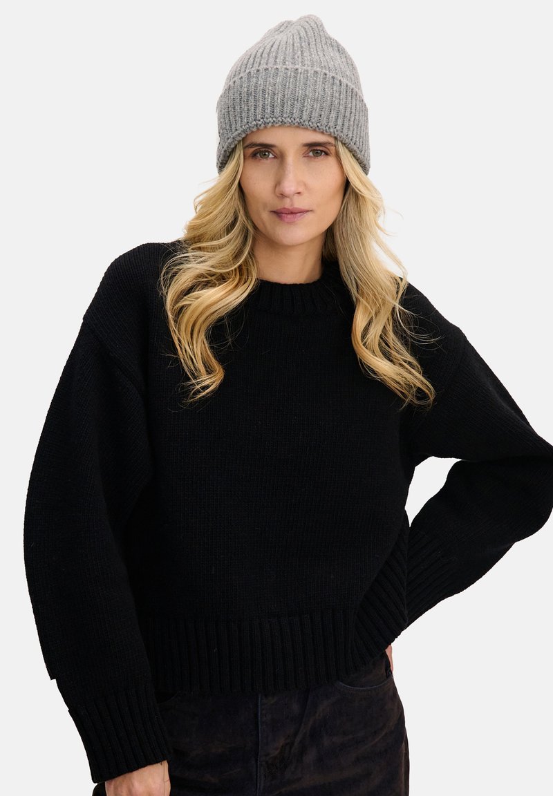 Czarny sweter z dzianiny z prążkowanym obszyciem, zestawiony z jasnoszarym prążkowanym beanie. Oba elementy mają przytulną fakturę i luźny fason.