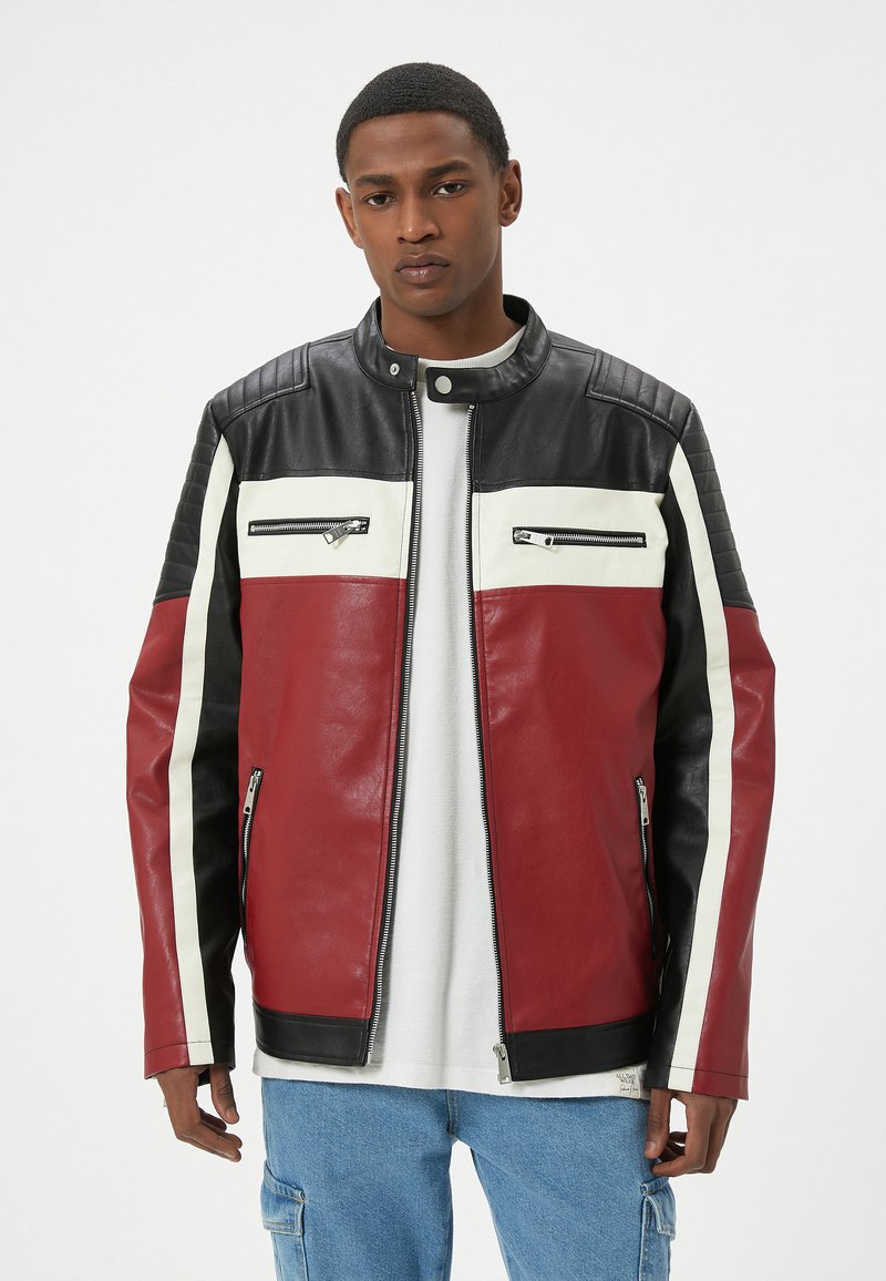 Giacca in pelle rossa e nera con strisce bianche, tasche con zip e dettagli trapuntati sulle spalle. Stile classico, texture sovrapposte.