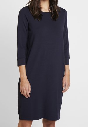 Granatowa sukienka do kolan z długimi rękawami, okrągłym dekoltem i bocznymi rozporkami. Wykonana z gładkiej, miękkiej tkaniny o luźnym kroju.