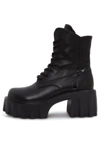 Stivale alla caviglia nero con lacci, realizzato in pelle sintetica lucida, con una suola platform spessa e un dettaglio accentuato sul tallone.
