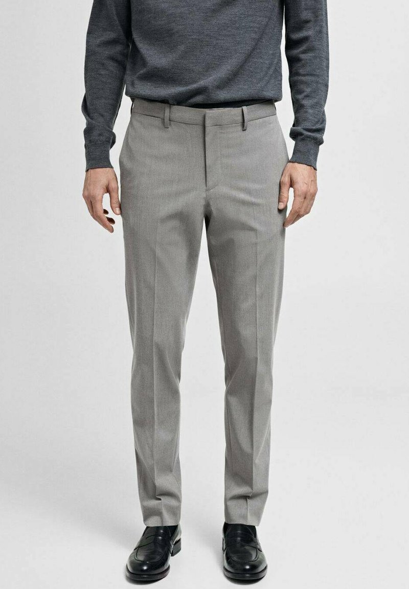 Pantaloni grigi su misura con una texture liscia, davanti piatto e passanti per la cintura, abbinati a un maglione scuro e scarpe nere lucide.