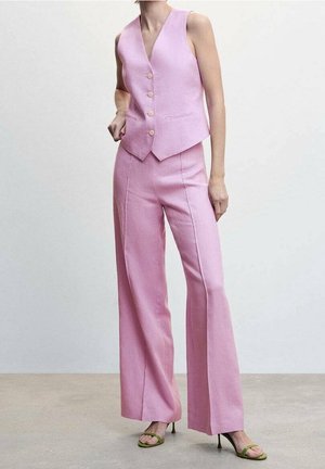 Femme portant un gilet rose sans manches ajusté avec des boutons et un pantalon large assorti, associé à des sandales à talons vertes.