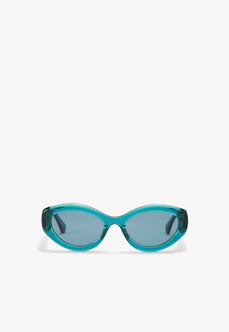 Une paire de lunettes de soleil bleu sarcelle avec une forme allongée œil de chat, une monture transparente et des verres teintés. Texture lisse avec des détails subtils sur les branches.