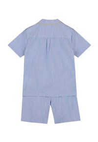 Ensemble de chemise à manches courtes bleu clair et de shorts assortis avec des détails de piping jaunes sur le col de la chemise, vu de dos.