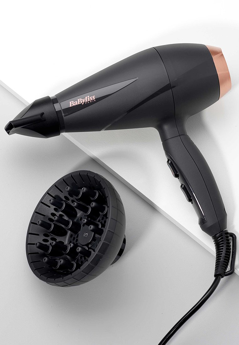 Sèche-cheveux noir avec un accent en or rose, équipé d'un buse et d'un diffuseur rond avec plusieurs pointes. Poignée texturée pour une prise en main.