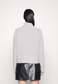 Ljusgrå ribbad tröja med hög hals, med sänkta axlar och en fåll som kontrasterar mot en svart läderkjol i miniformat.