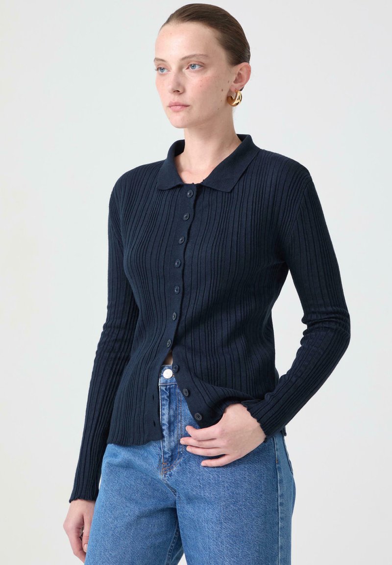 Mörkblå ribbad cardigan med krage, långa ärmar och knappstängning, ihop med blå jeans med hög midja.