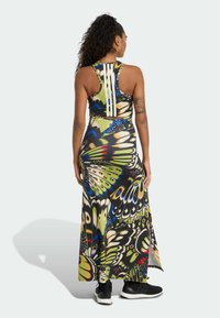 Robe maxi avec imprimé papillon, fond noir, accents verts et bleus. Dispose d'un dos nageur et d'une silhouette fluide, portée avec des baskets.