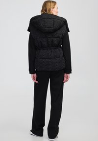 Czarna pikowana kurtka z fakturowanym kapturem, ściągnięta w talii, oraz długie czarne spodnie. Charakteryzuje się gładkim wykończeniem i minimalistycznym designem.