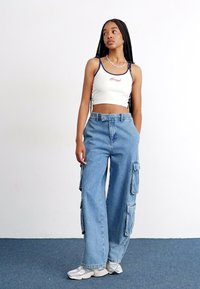 White cropped tank top with a logo, paired with light blue wide-leg cargo jeans featuring multiple side pockets and a relaxed fit.