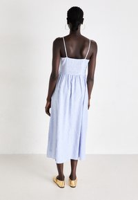 Sininen ja valkoinen raidallinen hihaton midi-mekko, jossa on kireä yläosa ja virtaava helma. Yhdistetty kultaisiin slip-on-kenkiin.