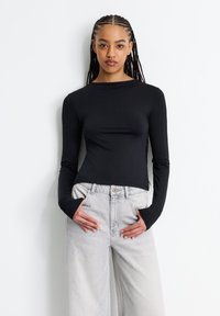 Schwarzes Langarmoberteil mit Rundhalsausschnitt und tailliertem Schnitt, kombiniert mit hellgrauen High-Waist-Jeans. Glatte Textur und minimalistischer Stil.