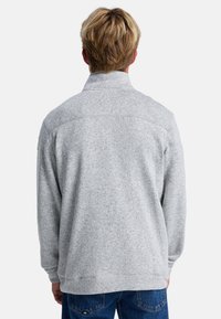 Sudadera de felpa gris con cuello alto, con un acabado texturizado. La prenda tiene mangas largas y un corte relajado.