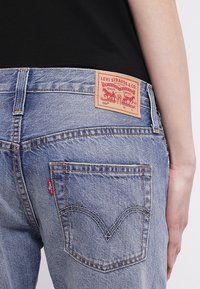 Vaaleansiniset farkut punaisella Levi's-tunnuksella takana, joissa on erottuva tikkaus taskuissa ja klassinen suora muotoilu.