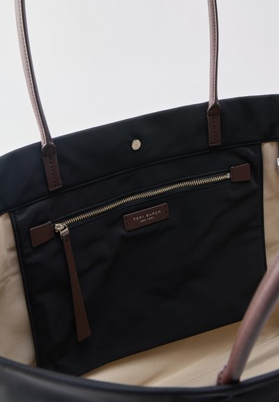 Vue intérieure d'un sac cabas noir et beige avec des poignées marron, comprenant une poche zippée et un patch logo Tory Burch New York.