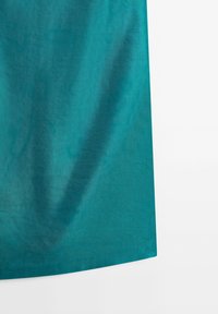 Teal-colored fabric with a smooth texture and slight wrinkles, set against a plain white background.