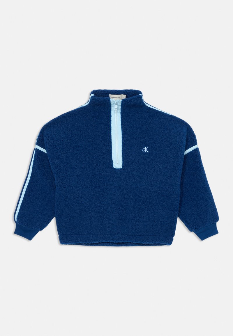 Temno modra flis majica s četrtinskim zadrgo spredaj, svetlo modri detajli na rokavih, rebrasti manšeti in izvezenim logotipom. Mehka, teksturirana tkanina.