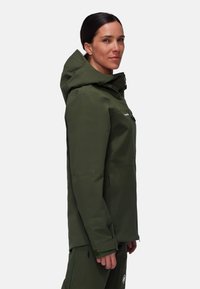 Giacca impermeabile verde oliva con cappuccio, chiusura a zip frontale e due tasche laterali. Presenta un tessuto liscio e polsini regolabili.