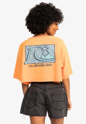 Cropped orange t-shirt featuring a blue graphic wave design and "Quiksilver" text on the back. Soft fabric with a relaxed fit.