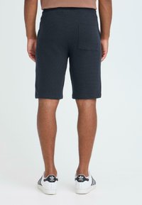 Shorts gris en tricot avec une surface texturée, dotés d'une ceinture élastique et d'une poche arrière, portés avec des baskets blanches.