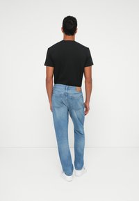 Camiseta negra de manga corta combinada con jeans de mezclilla azul claros, con un parche de cuero marrón en la parte trasera de la cintura y zapatillas blancas.