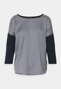 Marinblå och vit prickig topp med trekvartsärmar, rund halsringning och en slät textur. Mörka ärmar kontrasterar med det mönstrade kroppen.