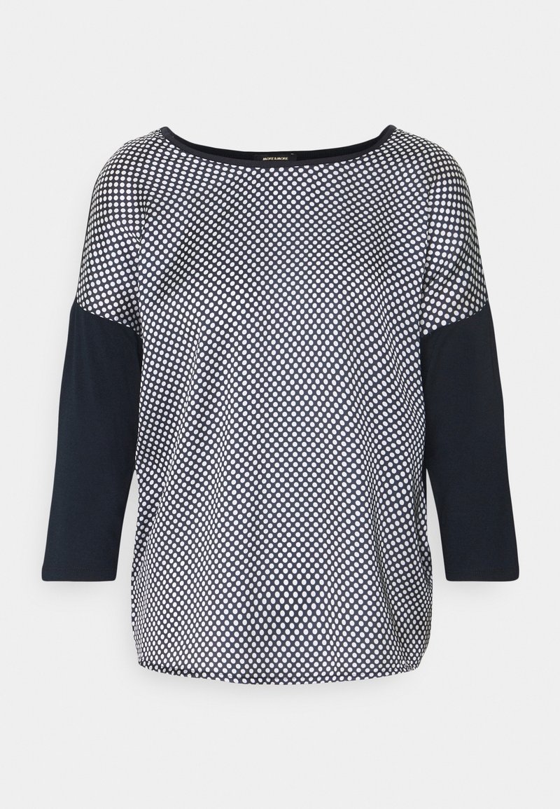 Marinblå och vit prickig topp med trekvartsärmar, rund halsringning och en slät textur. Mörka ärmar kontrasterar med det mönstrade kroppen.