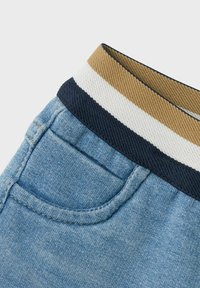 Jeans kratke hlače iz modrega blaga, z vzorčasto elastično pasom v rjavi, mornarsko modri in beli črtah ter detajlom na zadnjem žepu.