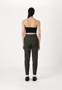 Top sans manches noir à rayures porté avec un pantalon ajusté vert foncé, présentant des poches latérales et une coupe légèrement fuselée.