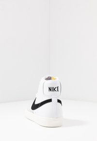 Vita höga sneakers med en svart swoosh, texturerad läder överdel, vadderad krage och Nike-logotyp på hälen. Gummisula.
