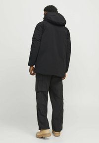 Sort puffjakke med hætte, kendetegnet ved en længere pasform og diskrete syninger. Kombineret med cargobukser og beige ankelstøvler.
