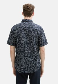 Chemise à manches courtes à boutons en bleu marine foncé avec motif botanique blanc. Tissu léger, coupe décontractée, ourlet arrondi, col classique, sans matériel visible.