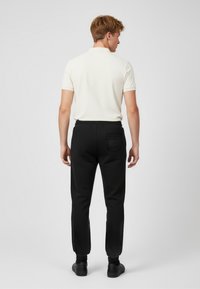 Męski strój składający się z kremowej koszulki polo i czarnych spodni dresowych z elastycznym pasem i boczną kieszenią. Gładka tkanina, swobodny krój.