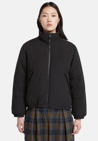 Giacca a vento nera con colletto alto, chiusura con zip frontale e polsini elasticizzati. Presenta una trama trapuntata e due tasche laterali con zip.