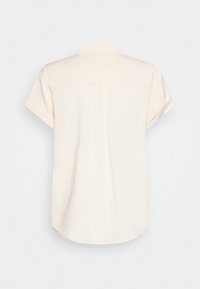 Chemise beige clair à manches courtes avec un col classique, une texture lisse, une couture du empiècement au dos et un ourlet arrondi. Aucun motif ni élément métallique visible.