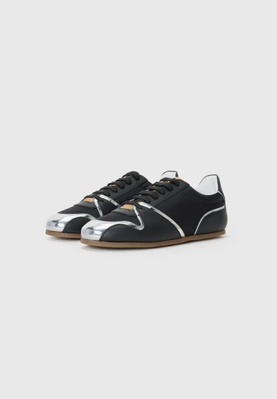 Black shoes with a metallic silver toe cap and accents, featuring a smooth texture, round shape, and flat brown sole. Laced design.