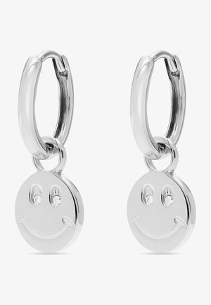 Orecchini a cerchio in argento presentano un ciondolo a forma di faccina sorridente con due piccole gemme trasparenti per occhi e una finitura liscia e lucida.