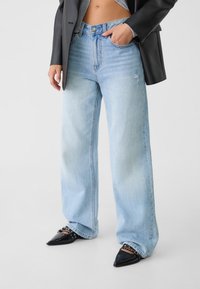 Ljusblå vida jeans i denim med en blekt finish och slitna detaljer, kombinerat med svarta spetsiga klackskor och en svart blazer.