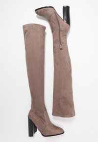 Botas de ante por encima de la rodilla en color topo con un diseño elegante, que cuentan con una cremallera lateral y un grueso tacón alto negro.