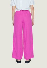 Pantaloni ampi di un vivido rosa, realizzati in un morbido tessuto testurizzato con vita elastica. Abbinati a calzature nere. Vista posteriore mostrata.